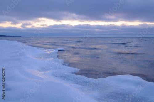 ice and snow on a beach in the foreground, clouds and a streak of light in the background © Kilman Foto