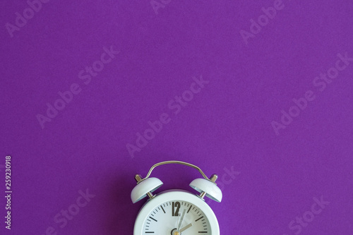 Flat lay of small alarm clock on purple background