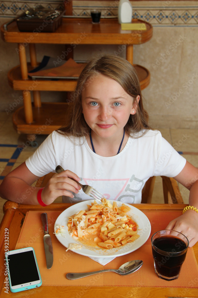 Modern child eating lunch with macaroni with sauce at restaurant