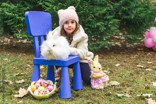 Wallpaper Mural Cute little girl having fun in the garden with Easter bunny sitting on the blue chair. Toy and basket with colored eggs and yellow chick toy on the grass. Easter concept Torontodigital.ca
