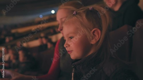 Mom and her little daughter are watching a performance at the circus, joyfully clapping their hands.