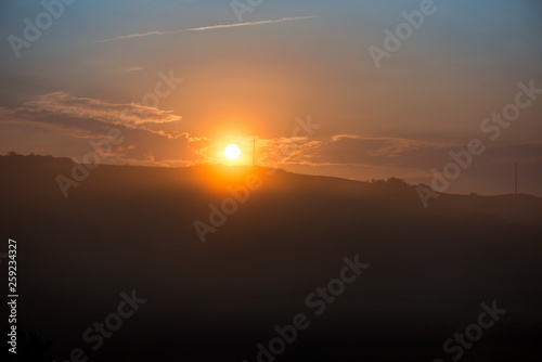 Beautiful morning in mountains. Thick fog covering the hills. Sunlight and rays trying to break through haze and trees