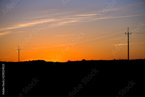A silhouette of high voltage electrical poles next to highway road on sunrise or sunset night sky background. Electricity wires and power lines. Ecological life. Beautiful nature landscape © lainen