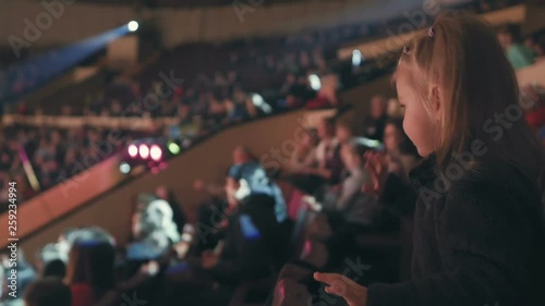 Mom and her little daughter are watching a performance at the circus, joyfully clapping their hands.