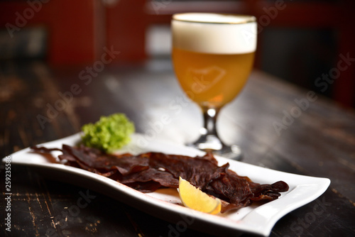 jerky with lemon and herbs on a white plate on the background of a glass of beer  basturma