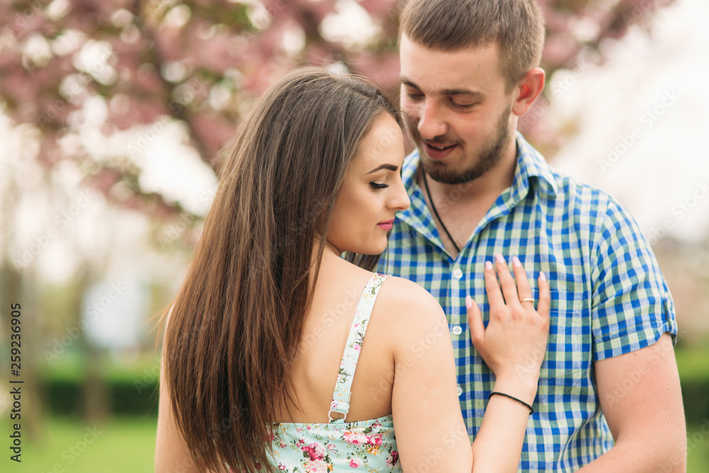 Portrait of young couple in spring mood. Blooming trees around man and woman Portrait of young couple in spring mood. Blooming trees around man and woman