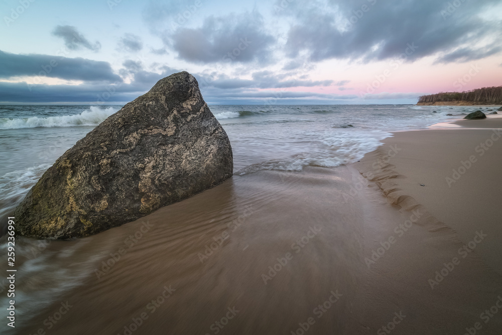 Big granite rock on the sandy beach of a Baltic sea at sunset