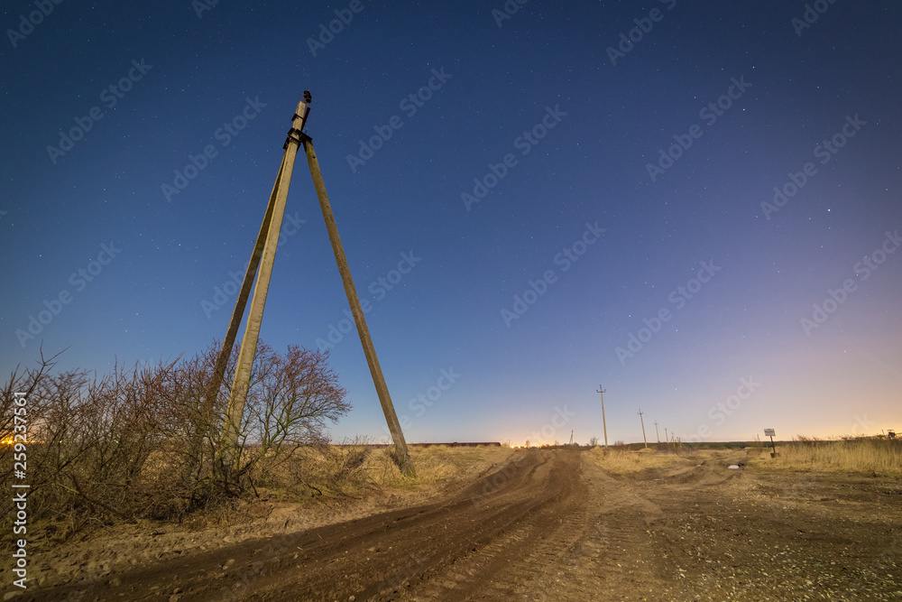 Fototapeta premium Dirt road and old power line towers at night