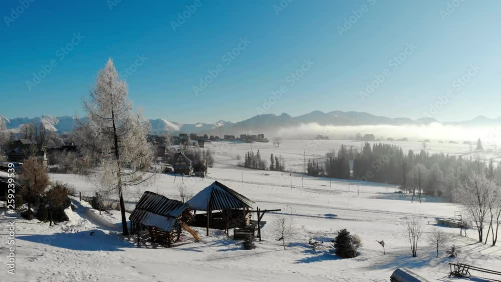 Aerial view of aged wood buildings on snowy terrain in mountains with bright blue sky Aerial view of aged wood buildings on snowy terrain in mountains with bright blue sky
