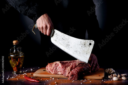Butcher cuts fresh meat on the wood board.Beef steak and salt on background with free space for text design or logotype menu restaurant.