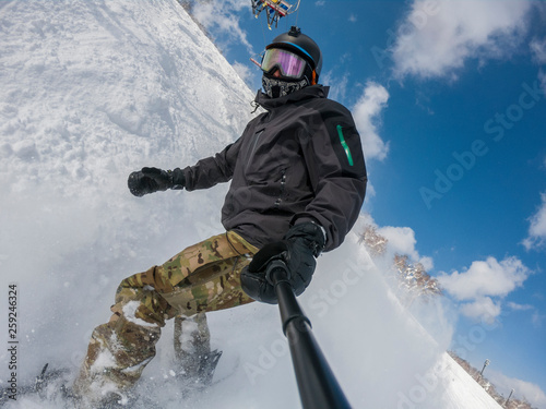 A snowboarder with action cam taking selfie on a ski slope at the Niseko