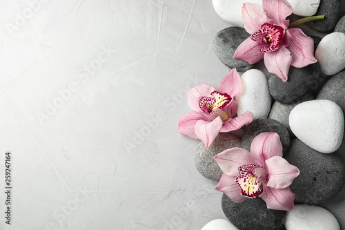 Fototapeta Naklejka Na Ścianę i Meble -  Zen stones and exotic flowers on grey background, top view with space for text