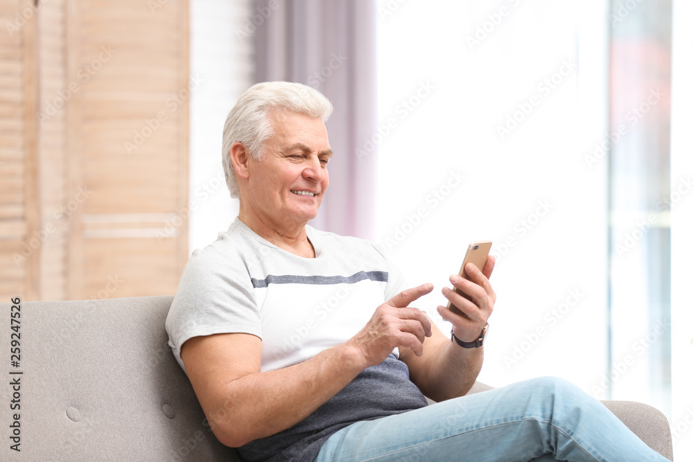 Portrait of mature man with mobile phone on sofa indoors Portrait of mature man with mobile phone on sofa indoors