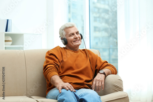 Portrait of mature man with headphones on sofa indoors