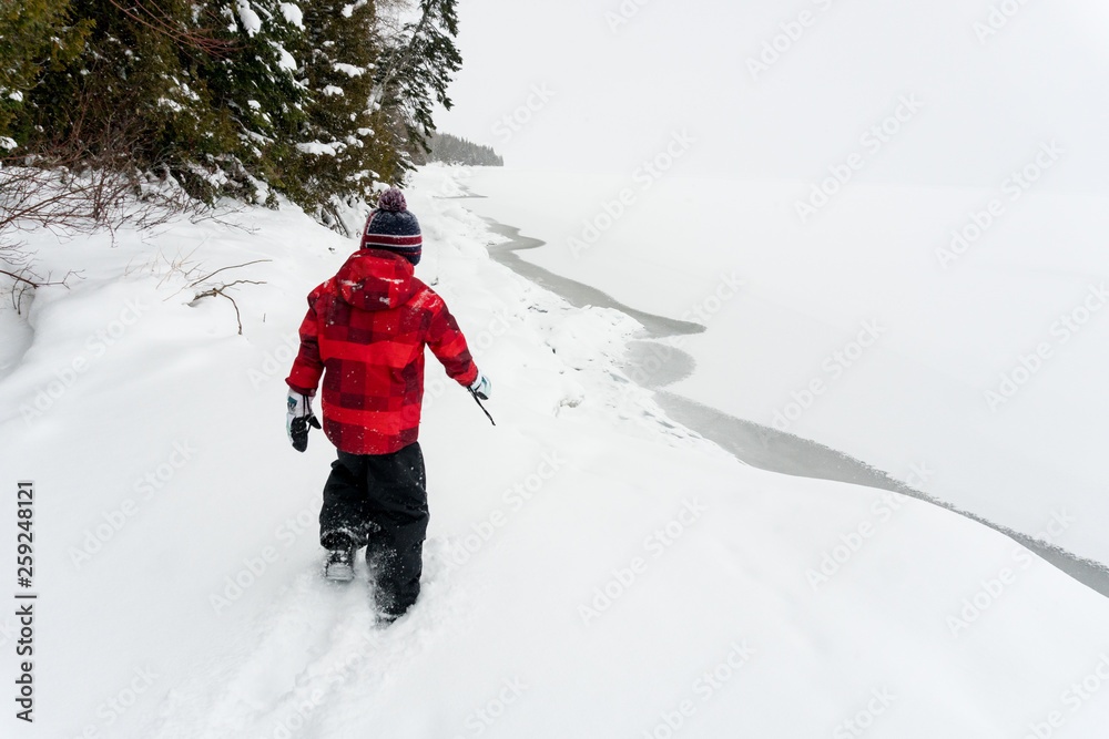 Boy walks alone in Ontario deep snow near edge of frozen lake Boy walks alone in Ontario deep snow near edge of frozen lake