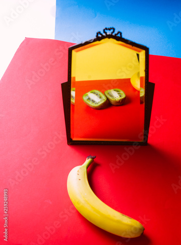 Banan fruti eflecting as sliced i on a mirror in a colored environemnt, conceptual image for the theme of changing , thinking difference, getting another identity, lost of himself photo