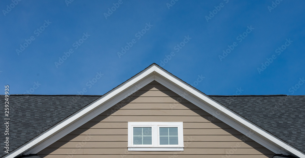 Attic window vent on brown siding, gable, corbel, louver on a new construction luxury American single family home in the East Coast USA with blue sky background