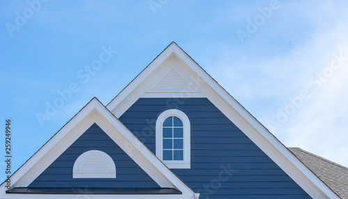 White attic window vent on blue siding, gable, corbel, louver on a new construction luxury American single family home in the East Coast USA with blue sky background