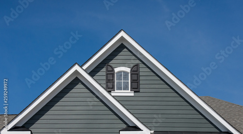 Attic window with black shutter on grey blue siding, gable, corbel, louver on a new construction luxury American single family home in the East Coast USA with blue sky background