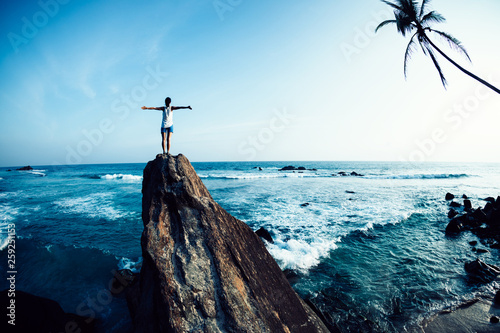 Successful woman outstretched arms on seaside rock cliff edge