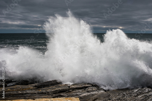 A large wave crashes over the rocks along the coast in Maine