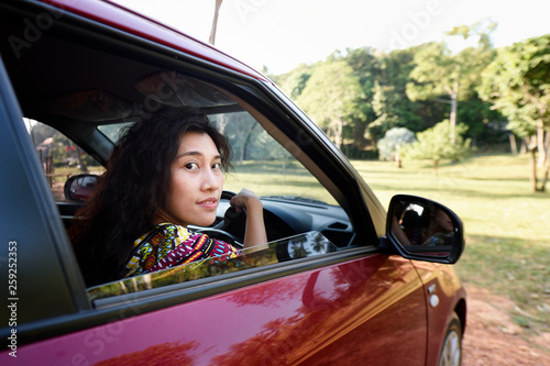 Trendy young woman driving a car on a topical road trip