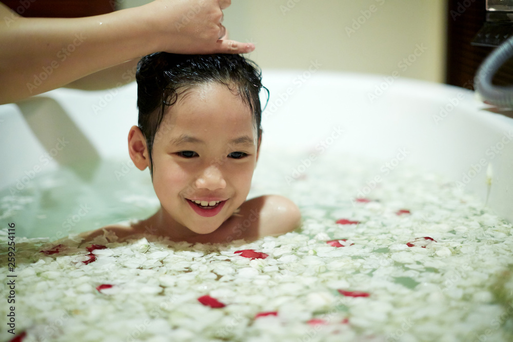 Cute Asian little girl bathing in a bathtub full of petals. foto de