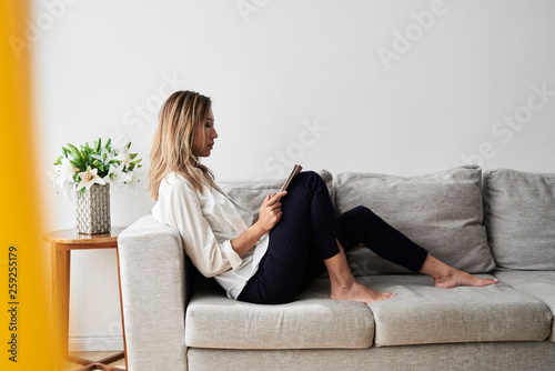 Asian woman reading on sofa.