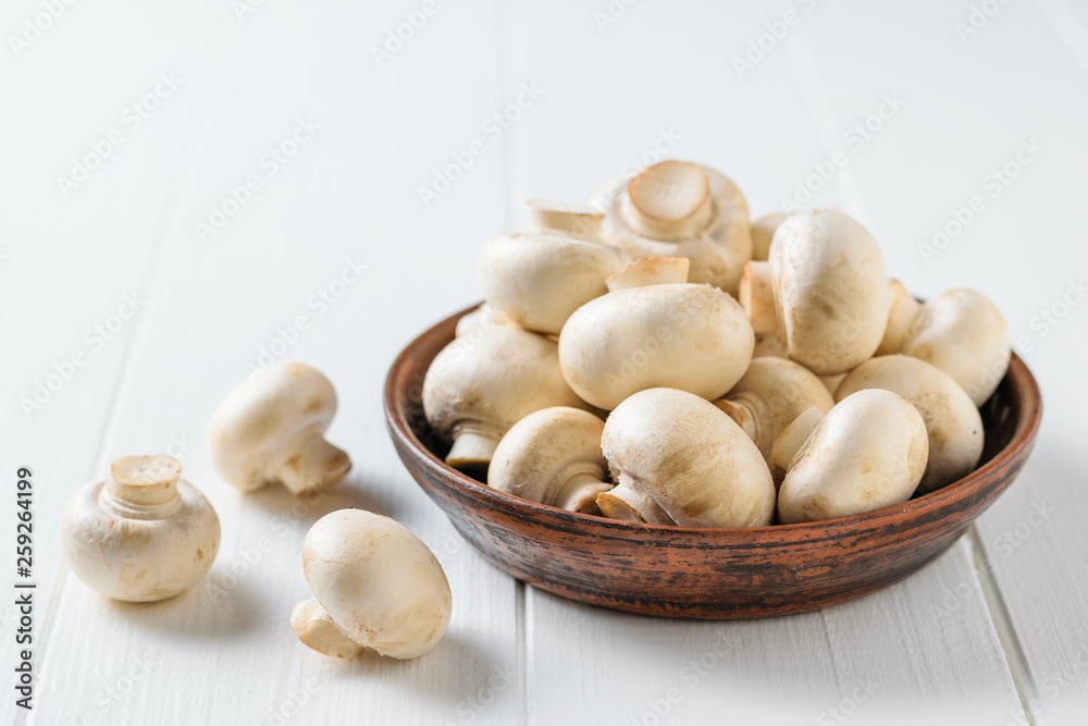 Clay bowl filled with fresh mushrooms on a white wooden table. Vegetarian cuisine. Clay bowl filled with fresh mushrooms on a white wooden table. Vegetarian cuisine.