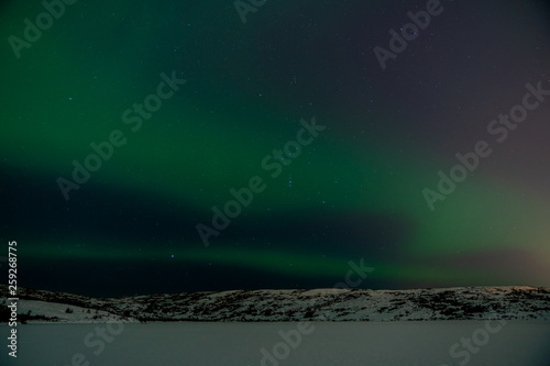 Northern lights and stars over snowy mountains and frozen lake