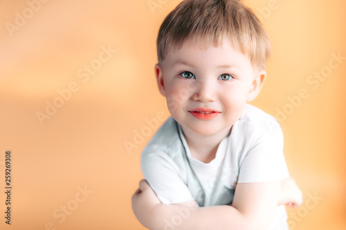 Portrait of blonde happy joyful beautiful cute little boy looking at camera on orange background