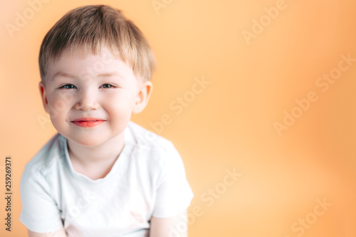 Portrait of blonde happy joyful beautiful cute little boy looking at camera on orange background