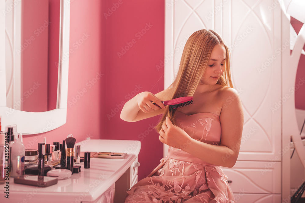 Teenage girl in a dress combing her hair in the bedroom Teenage girl in a dress combing her hair in the bedroom