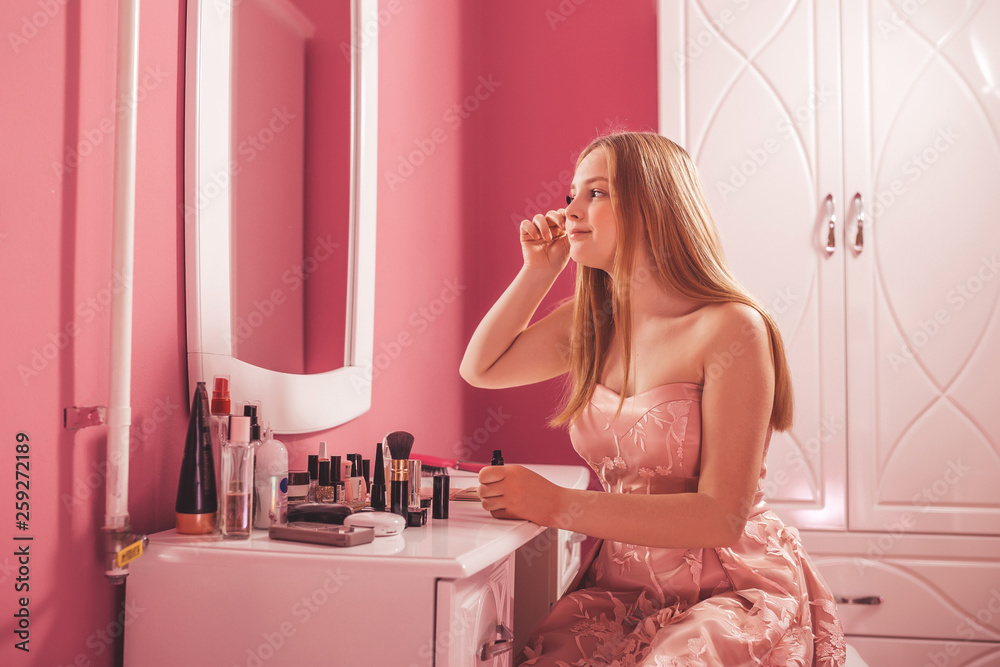 Teenage girl in a dress applying makeup on face at home