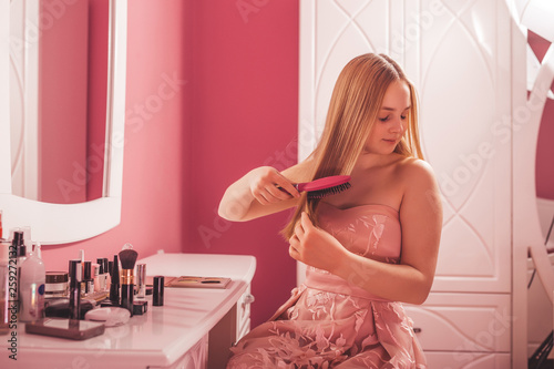 Teenage girl in a dress combing her hair in the bedroom