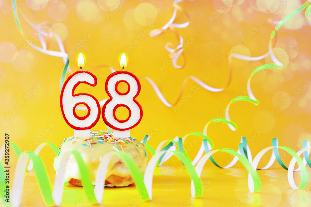 Sixty eight years birthday. Cupcake with burning candles in the form of number 68. Bright yellow background with copy space