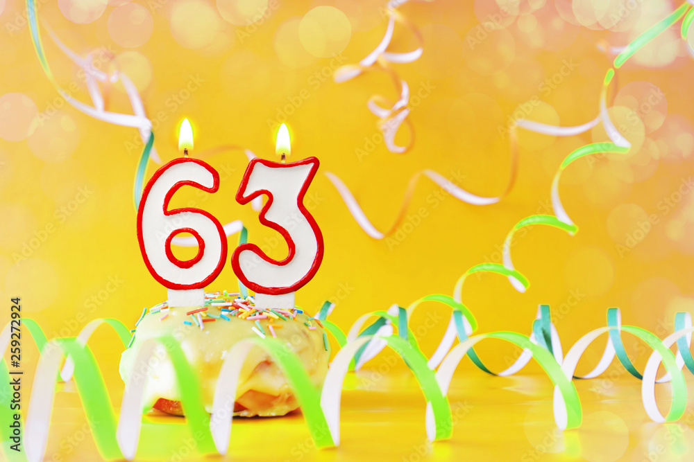 Sixty three years birthday. Cupcake with burning candles in the form of number 63. Bright yellow background with copy space