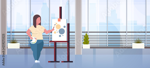 fatty obese woman painter holding paintbrush overweight girl artist painting process modern art workshop studio interior full length flat horizontal