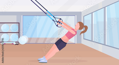 sporty woman doing exercises with suspension fitness straps elastic rope girl training crossfit workout concept modern gym studio interior horizontal flat full length