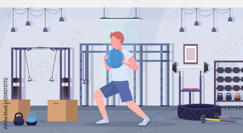 sporty man doing crossfit exercises running with medicine leather ball guy training cardio workout concept modern gym health studio club interior horizontal full length