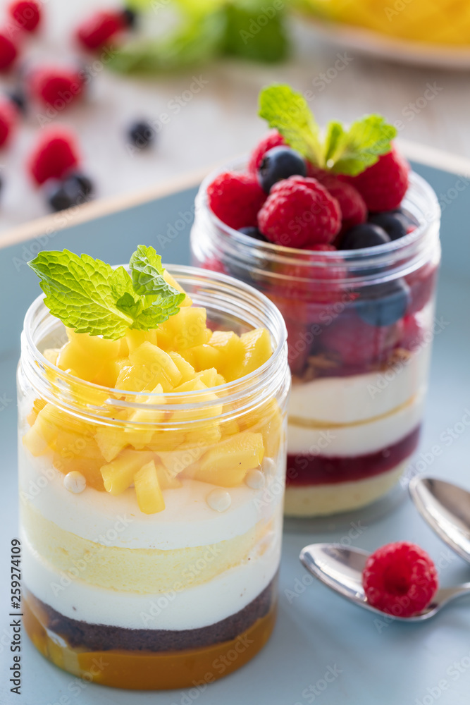 Raspberry and mango dessert, cheesecake, trifle, mouse in a glass jar on a light wooden background, vertical composition Raspberry and mango dessert, cheesecake, trifle, mouse in a glass jar on a light wooden background, vertical composition