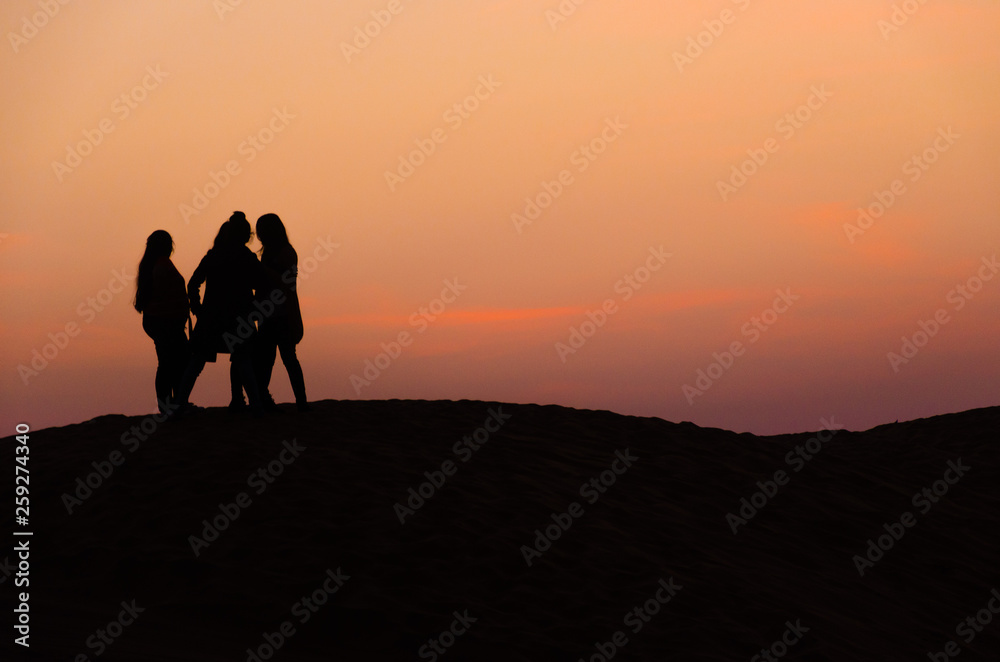 silhouette of three friends in beautiful evening in desert
