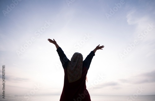 Unidentified silhouette happiness and joyful woman girl rise hand up during oceanview on blue sky background - Image