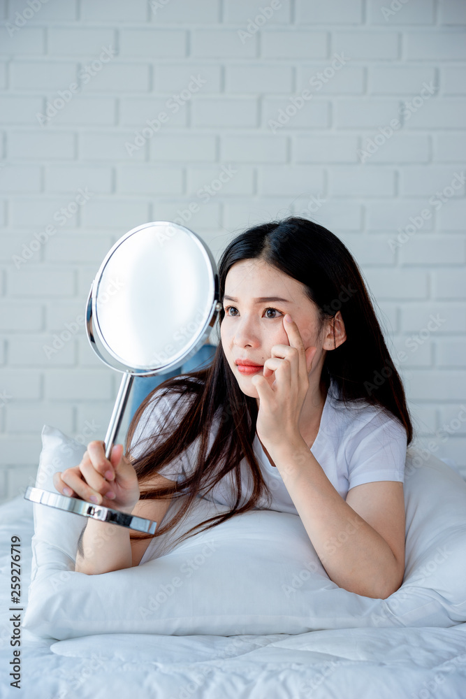 Asian teenage woman looking at mirror and squeeze acne problem on her face, skin care concept. Asian teenage woman looking at mirror and squeeze acne problem on her face, skin care concept.