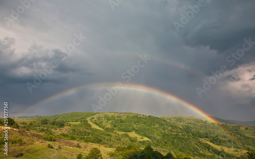 Beautiful mountain valley with green hills and huge rainbow