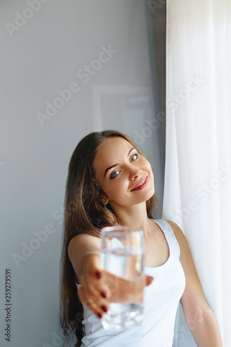 Closeup young woman show glass of water. Portrait of happy smiling female model  holding transparent glass of water.Healthy lifestyle. Beauty  Diet concept