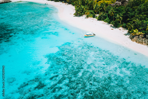 Aerial drone above view of paradise isolated beach. Lonely tourist boat in turquoise shallow lagoon ocean water surrounded by coconut trees
