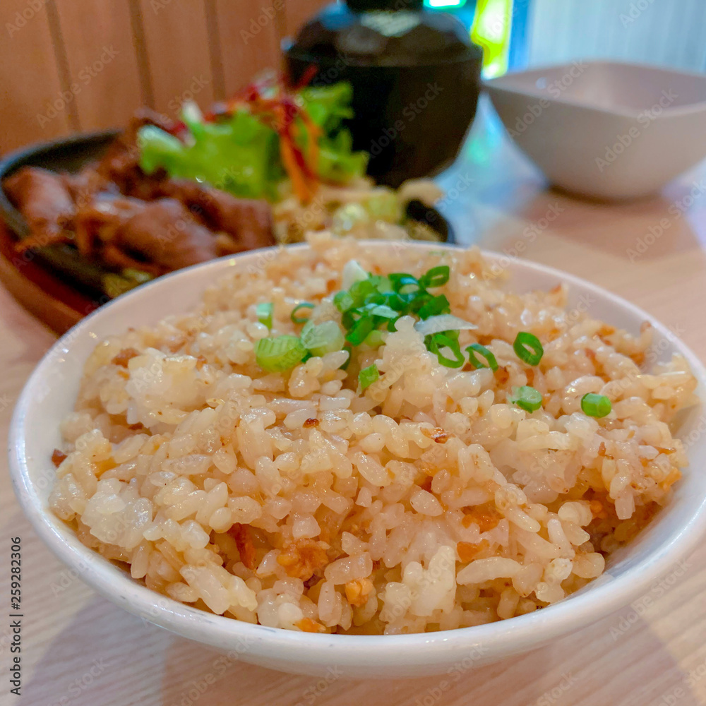 Garlic fried rice in a white ceramic bowl placed on a wooden table in a Japanese restaurant. Garlic fried rice in a white ceramic bowl placed on a wooden table in a Japanese restaurant.