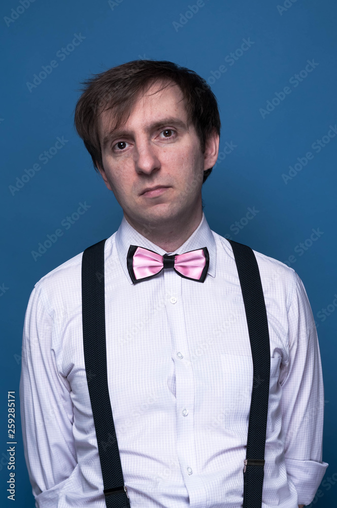 handsome man in shirt, pink bow tie and black suspenders looking at camera on blue background handsome man in shirt, pink bow tie and black suspenders looking at camera on blue background