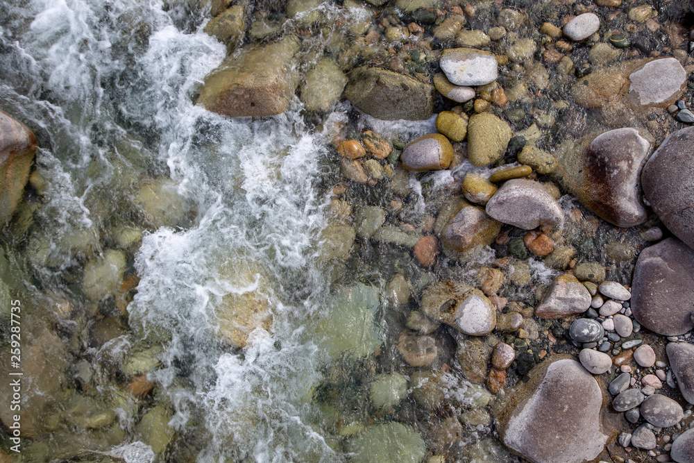 Water in the mountain raging river. Beautiful natural background of stones and water. Texture of clear water and fast river. Background to insert text. Tourism and travel. Water in the mountain raging river. Beautiful natural background of stones and water. Texture of clear water and fast river. Background to insert text. Tourism and travel.